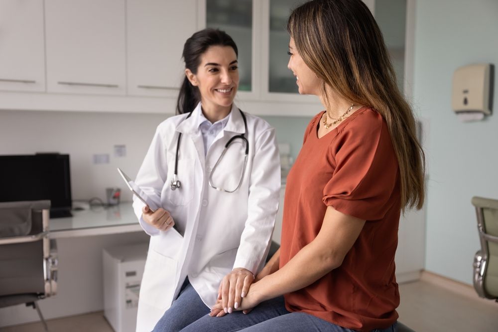 Doctor talking with seated patient in exam room, holding a clipboard.