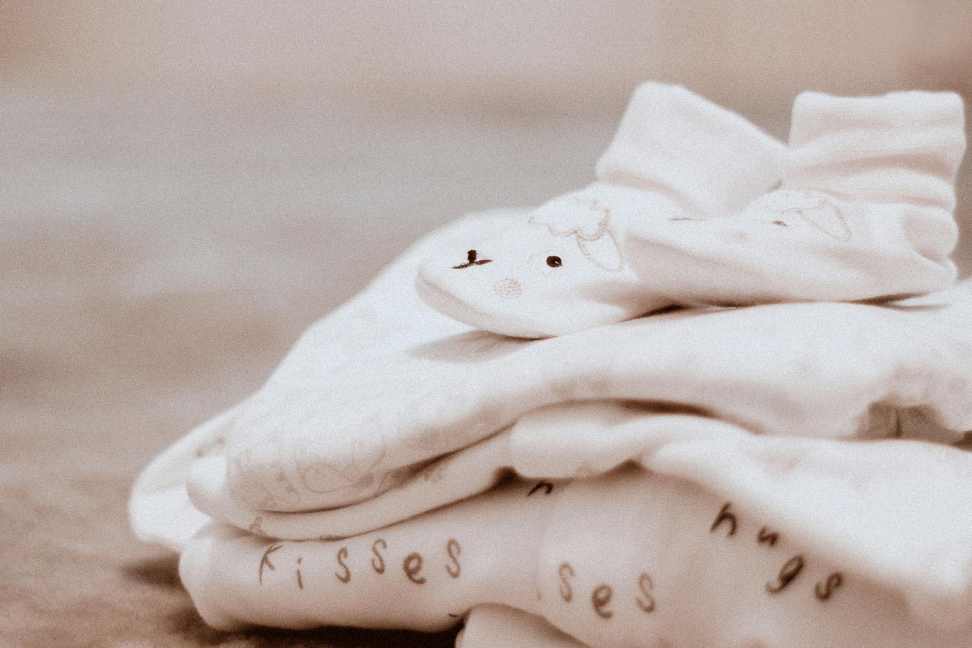 Stack of white baby clothes, including a onesie with 