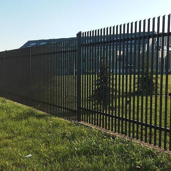 Black metal fence beside a grassy slope with a building in the background