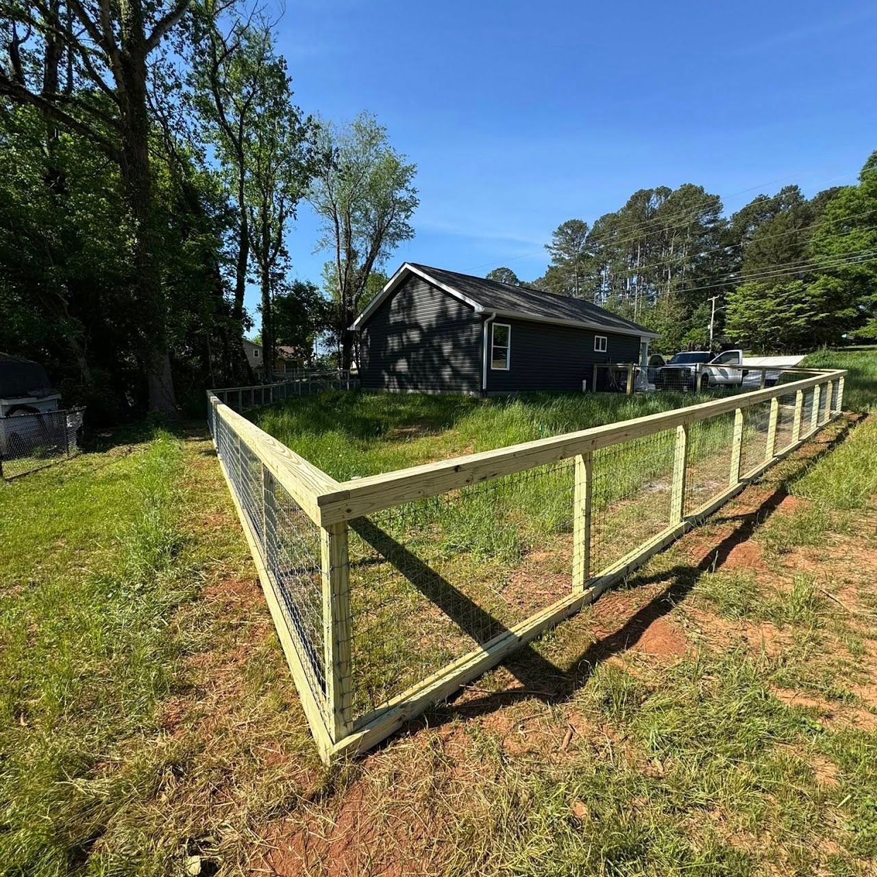 Wooden fenced yard beside a dark cabin in a sunny wooded rural area