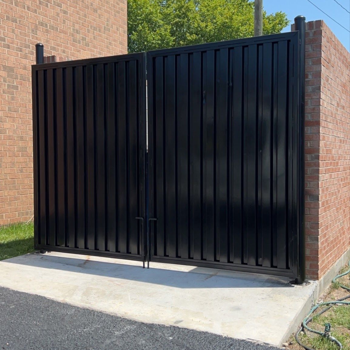 Black metal double gate between brick pillars at a driveway entrance