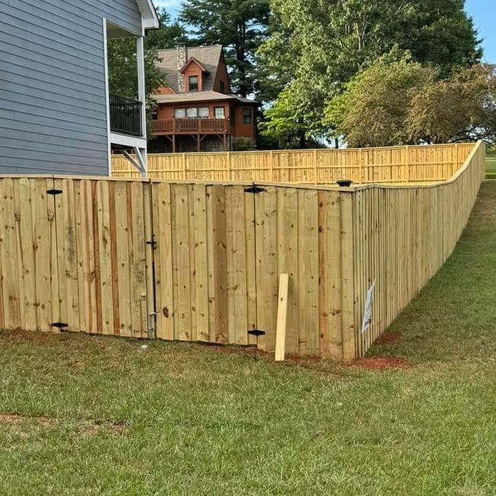 Wooden privacy fence enclosing a grassy yard beside a blue house, with trees and a house in the background