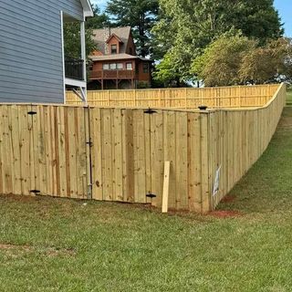 Wooden privacy fence enclosing a grassy yard beside a blue house, with trees and a house in the background