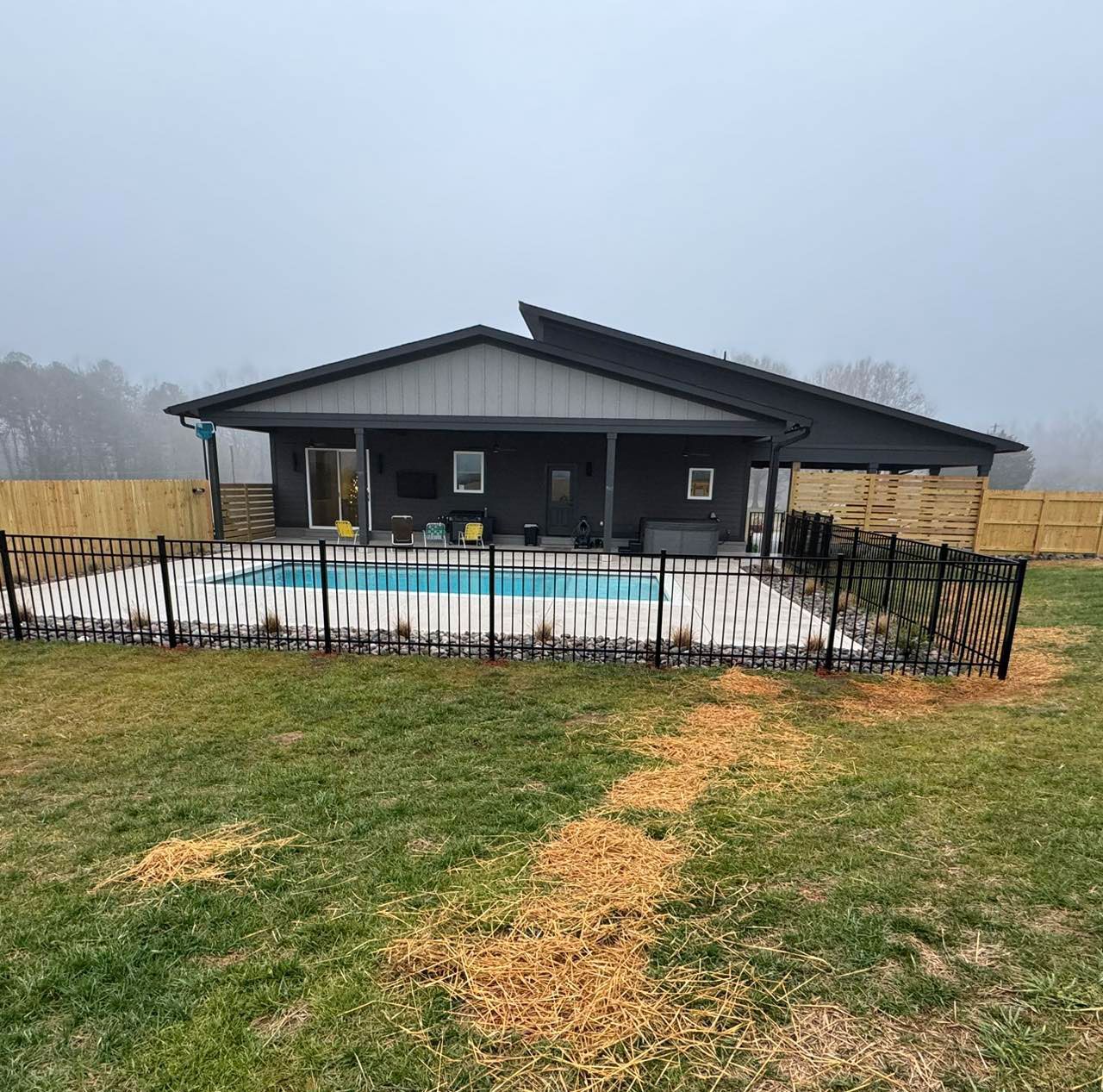 Modern black house with fenced above-ground pool in a grassy yard on an overcast day
