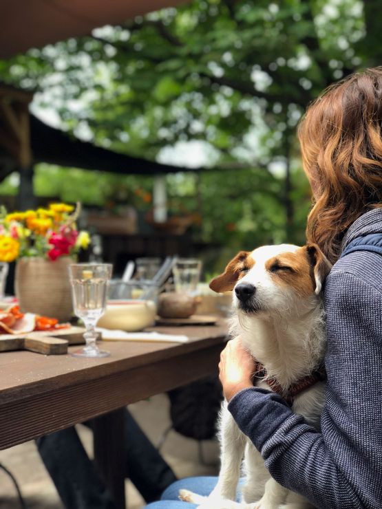 Woman holding a small dog at an outdoor café table with drinks and flowers
