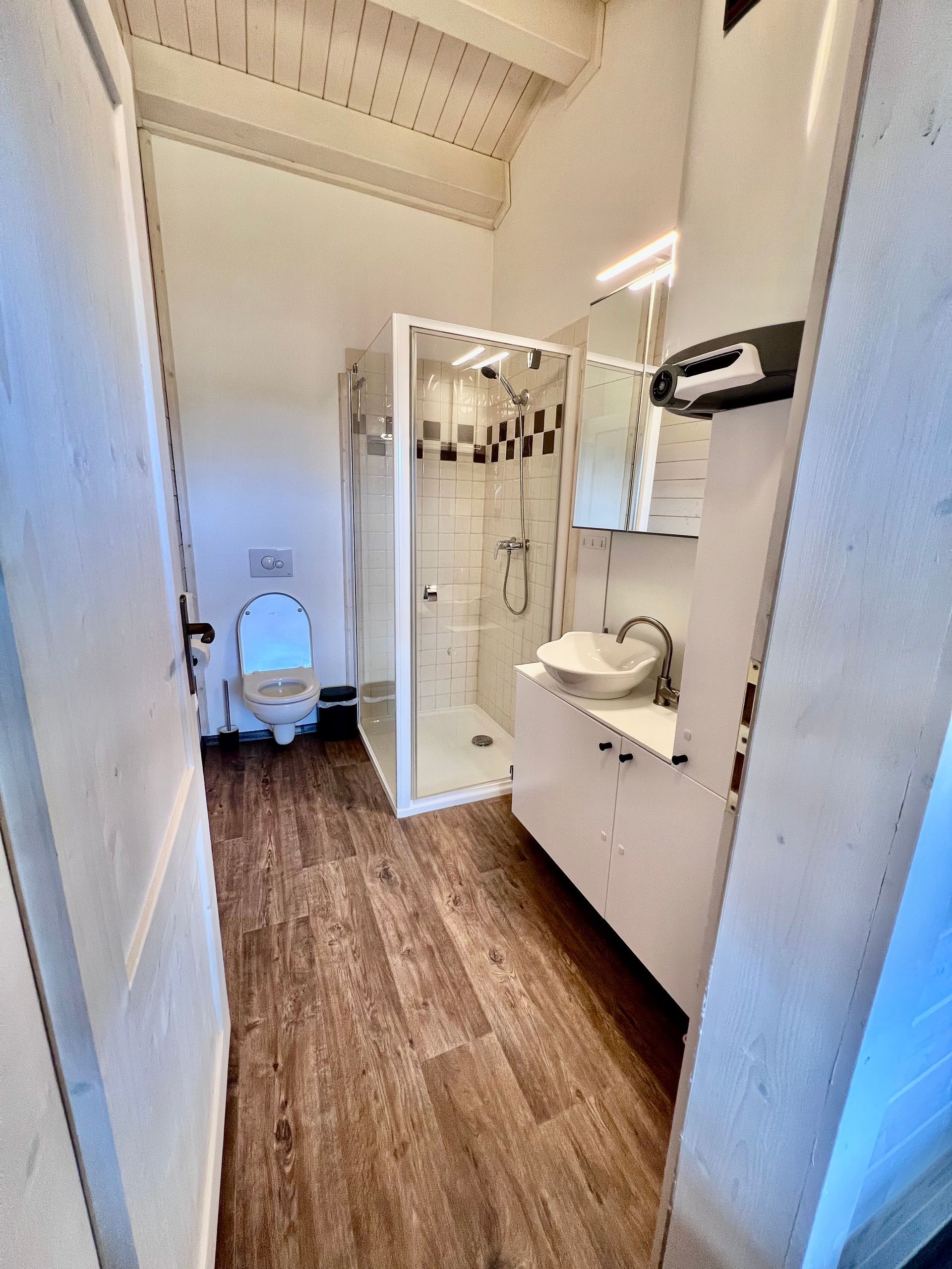 Small bathroom with a toilet, shower, and sink, brown floor and white walls.