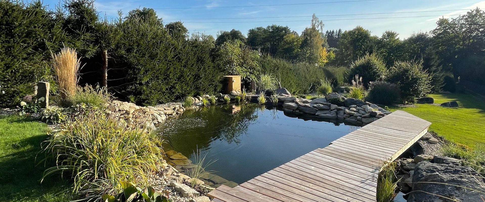 A scenic pond with a wooden bridge and surrounding lush greenery.