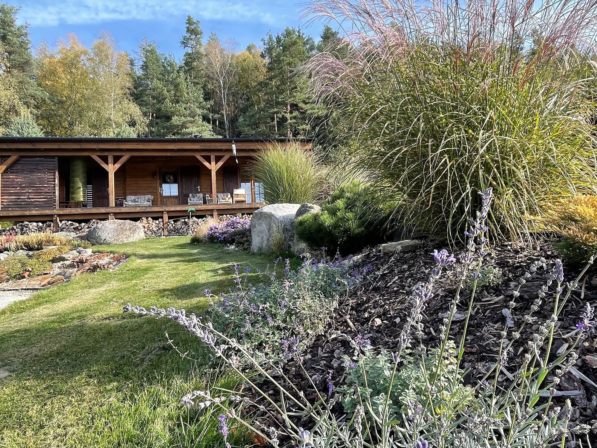 Wooden cabin with lush garden in foreground; trees in the background.