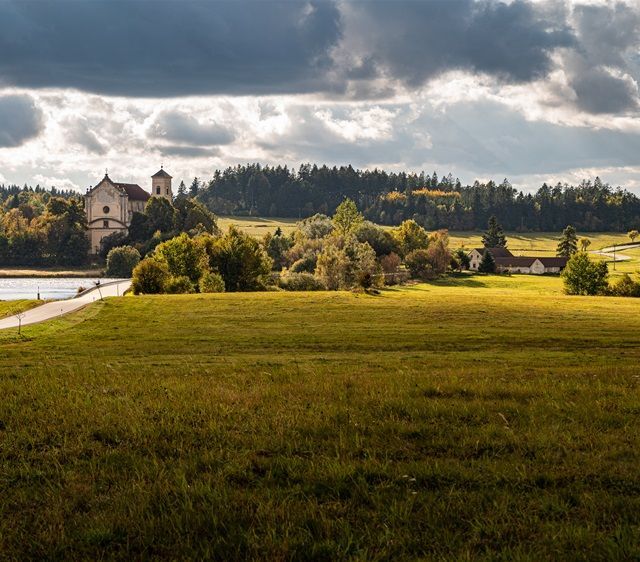 Green field, trees, and a light-colored building under a cloudy sky.