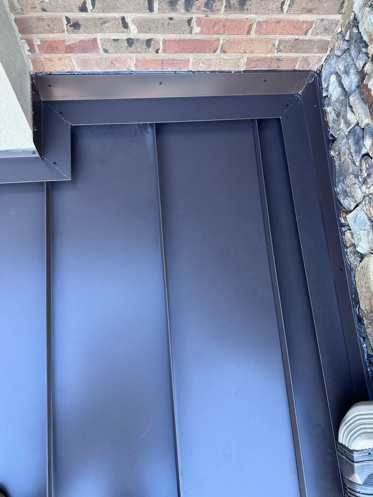 A high-angle view of a newly installed dark metal roof with precise flashing against a brick wall and stone siding.