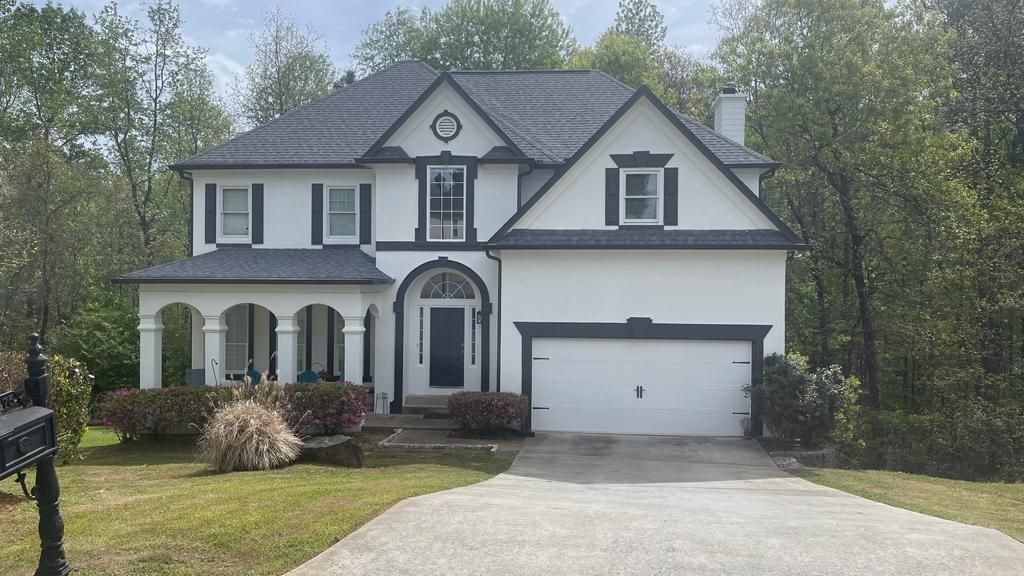 A white, two-story house with a black shingled roof, dark trim, a covered front porch, and an attached two-car garage.