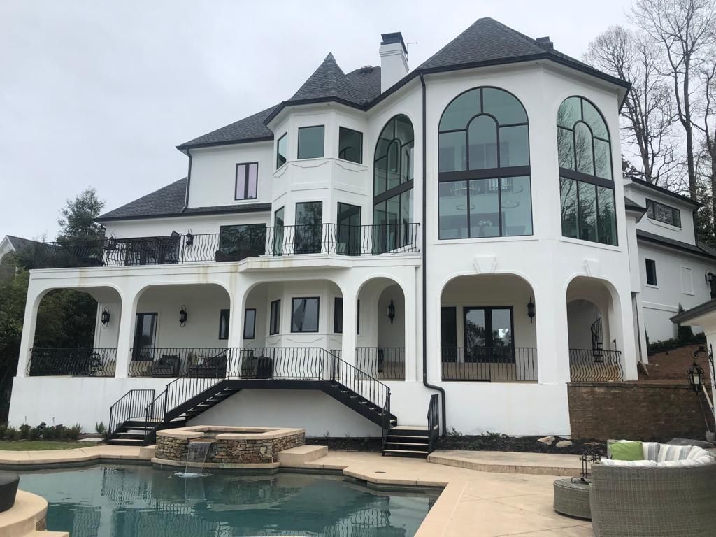 A white, multi-story Mediterranean-style home with arched patios and large windows overlooking a swimming pool.