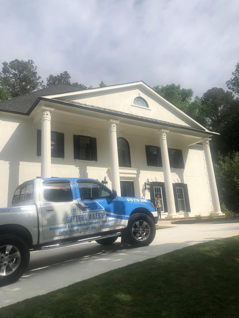 A silver and blue work truck parked in front of a white two-story colonial-style house with pillars.