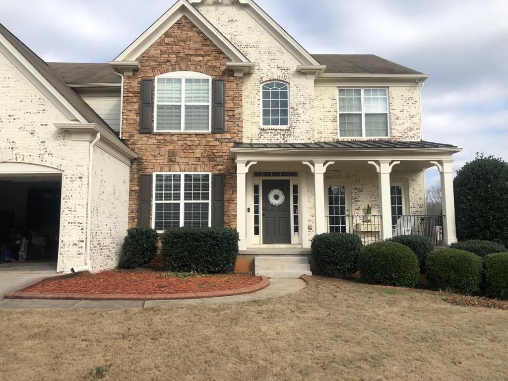Two-story suburban house with cream brick, a stone-accented front, a covered porch, and a brown front door.