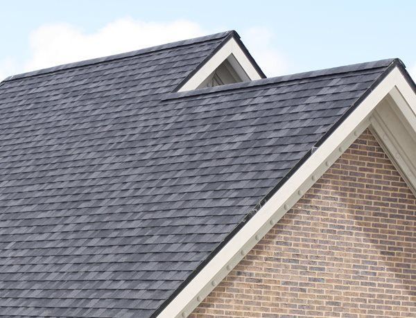 Gray shingled house roof with white trim and a brick gable under a blue sky