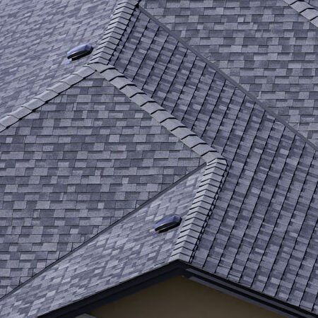 A close-up of a residential roof featuring gray, textured architectural shingles with two black vent covers.