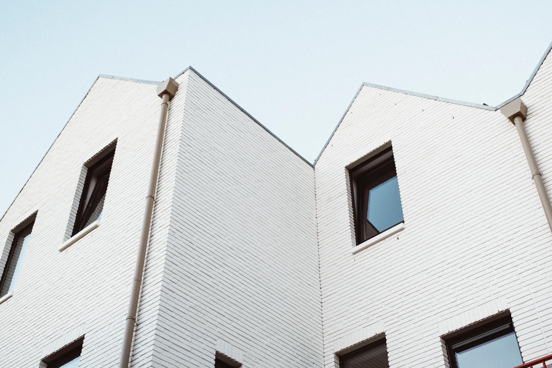 Low-angle view of two adjacent modern buildings with white brick facades, gabled roofs, and recessed dark-framed windows.