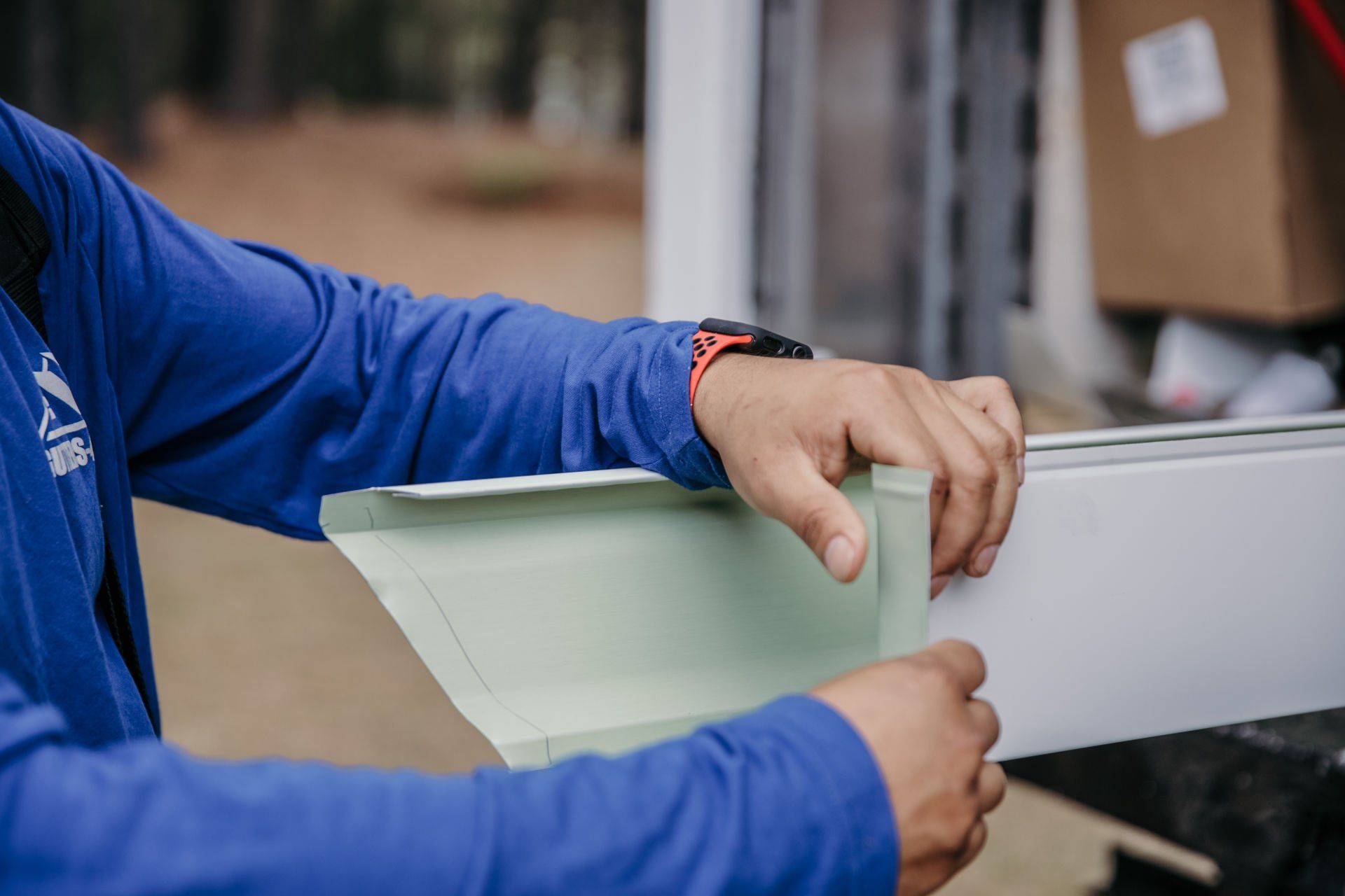 Hands in a blue shirt fit a light green gutter end cap onto a piece of white metal guttering.