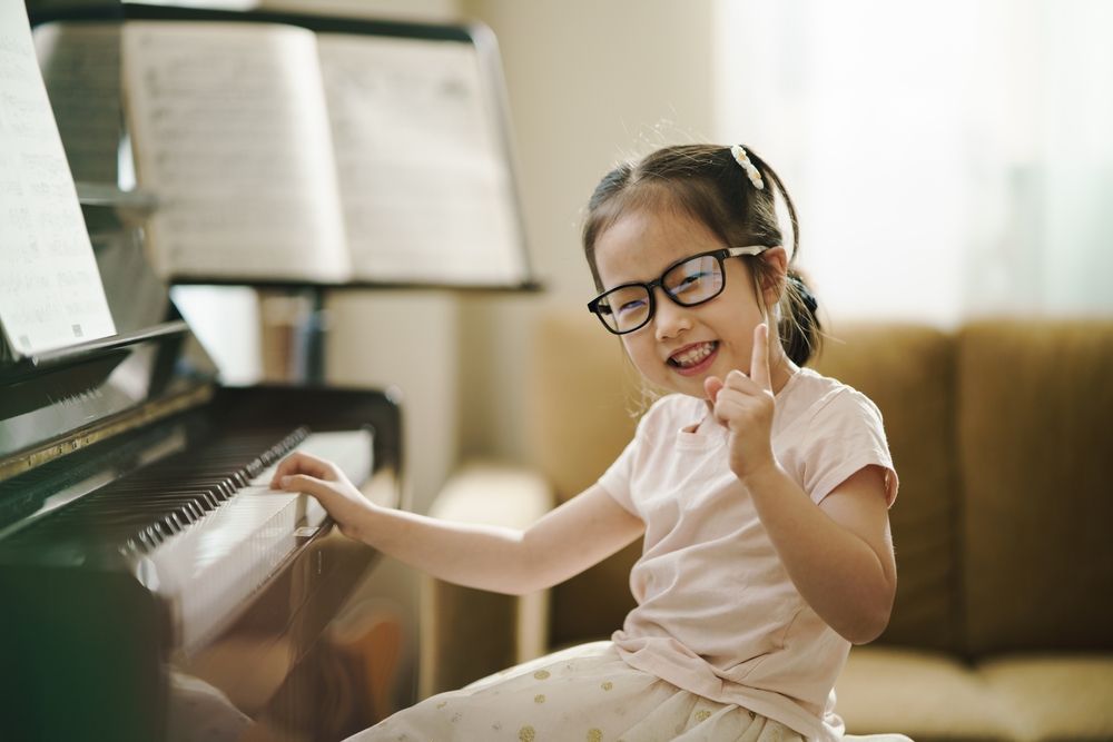 Child wearing glasses smiling while playing piano in a bright room