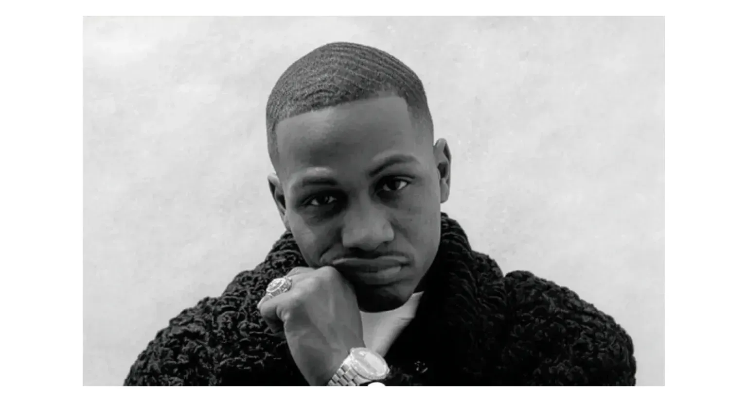 Portrait of a person resting their chin on a hand, wearing a dark textured sweater against a light background