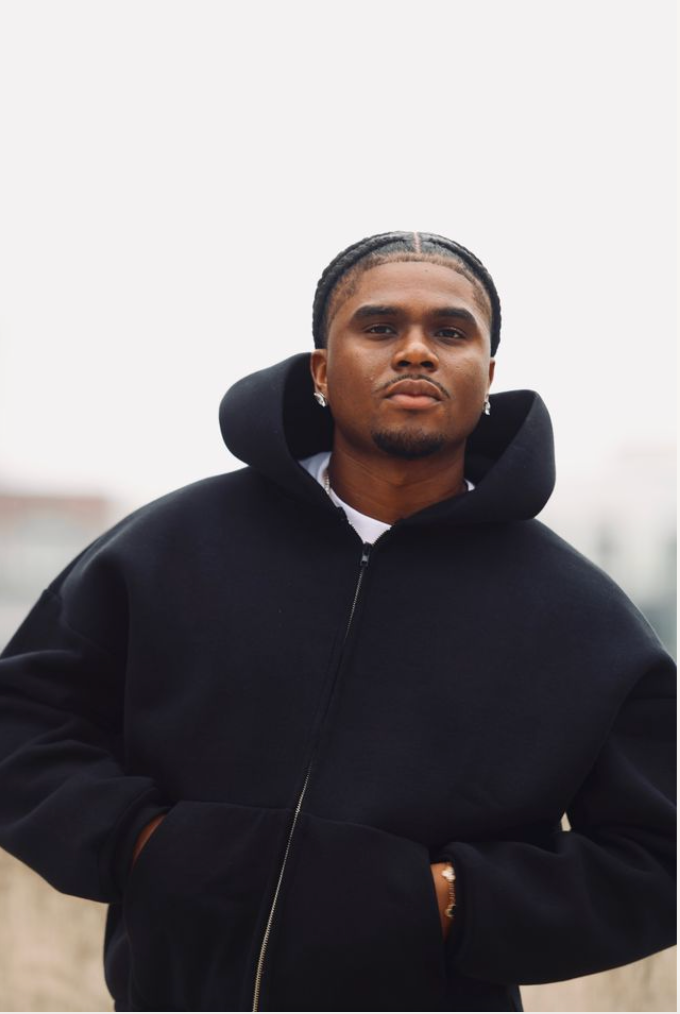 Person in a black hooded coat standing outdoors against a blurred background.