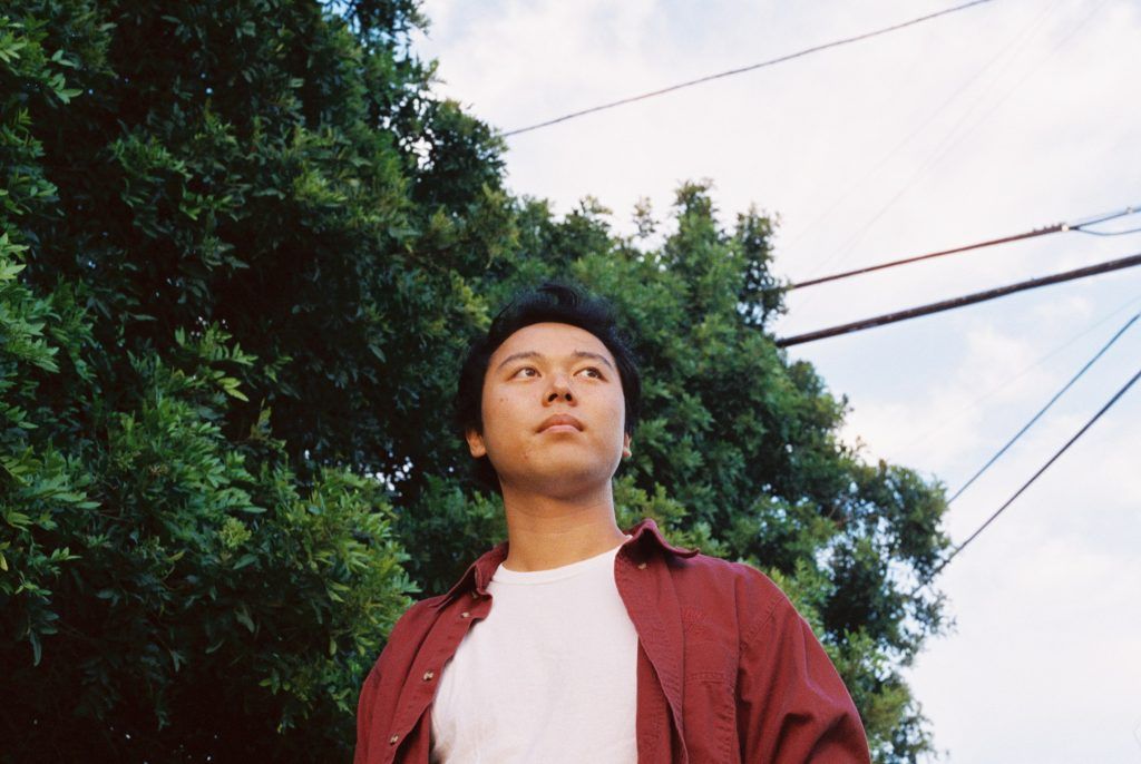 Person in a red jacket looking up outdoors near trees and power lines