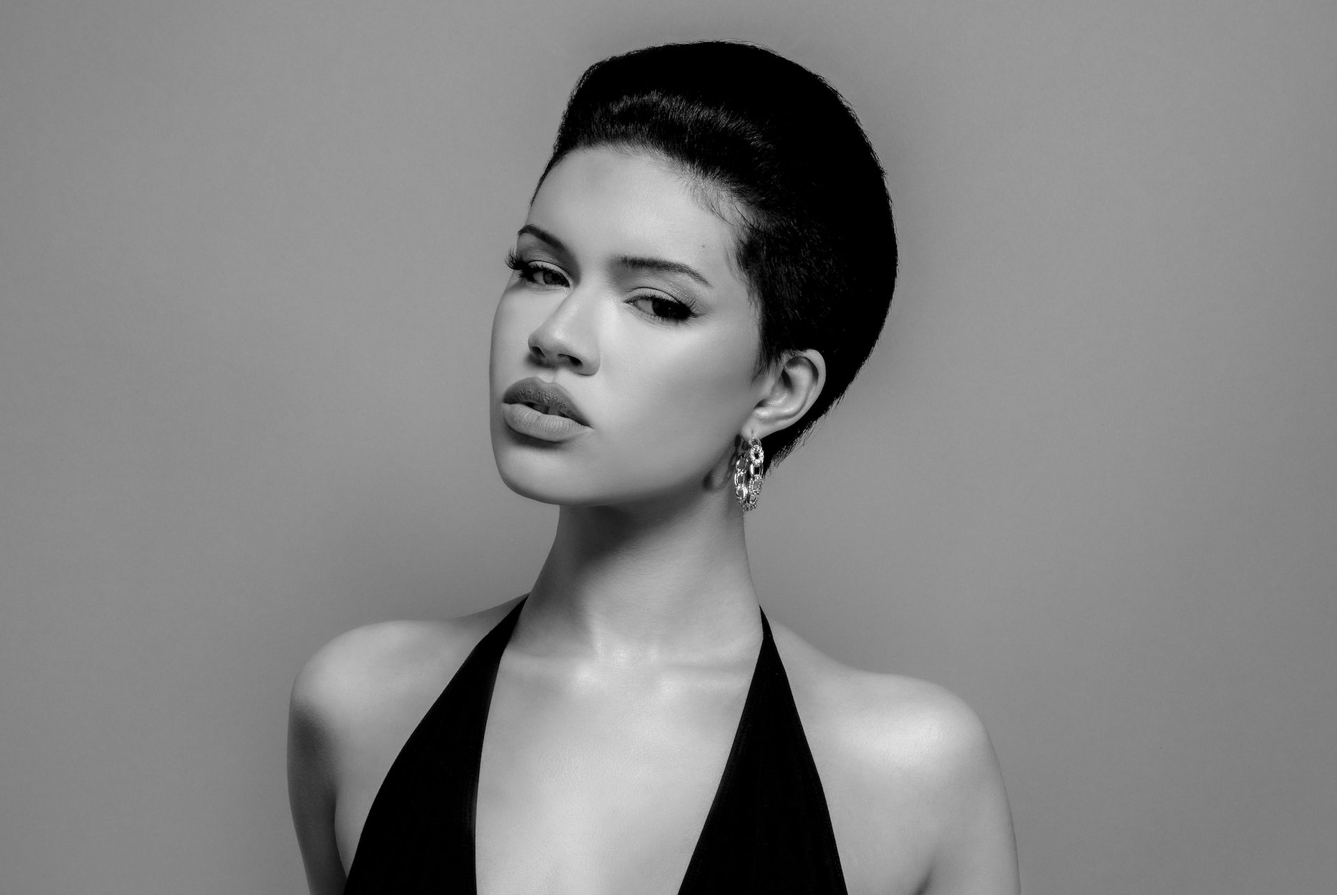Portrait of a person with short hair in a black halter top against a plain gray background