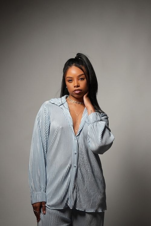 Person in a blue-and-white striped oversized shirt posing against a gray backdrop.