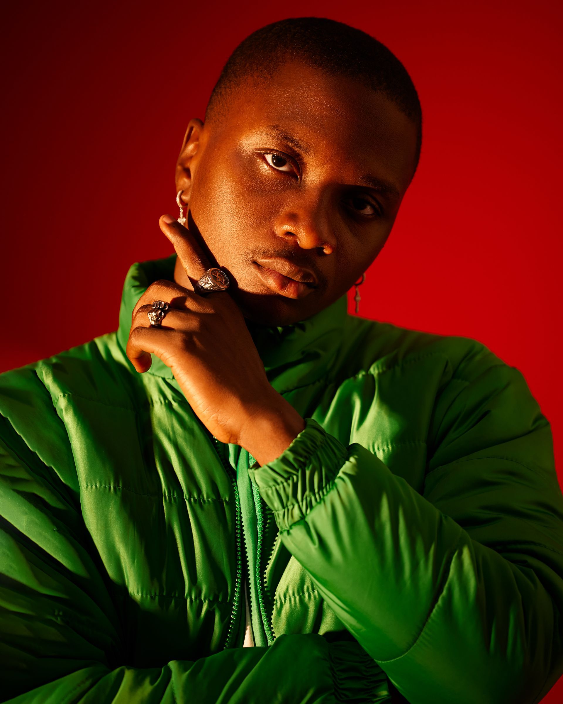Person in a bright green jacket posing against a red background, hand near face.