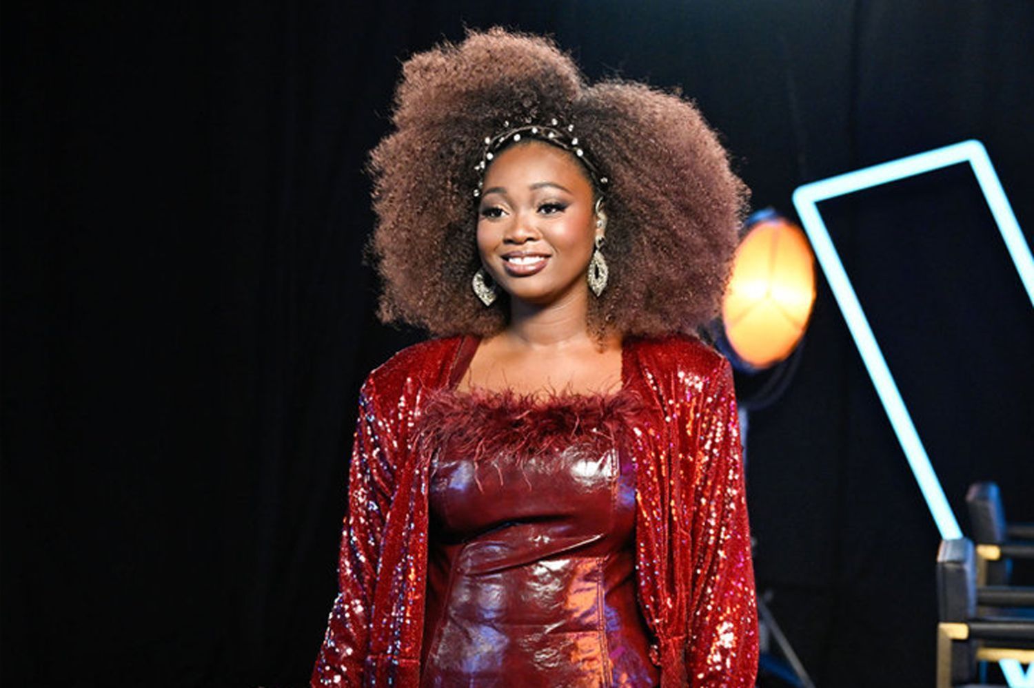 Woman in a red sequined outfit smiling on stage against a dark background