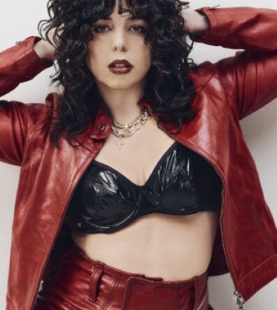 Person in a red jacket and pants with a black top, posing with hands behind head.