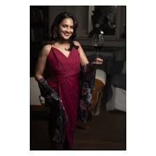 Woman in a burgundy dress and black gloves holding a glass in a dimly lit room