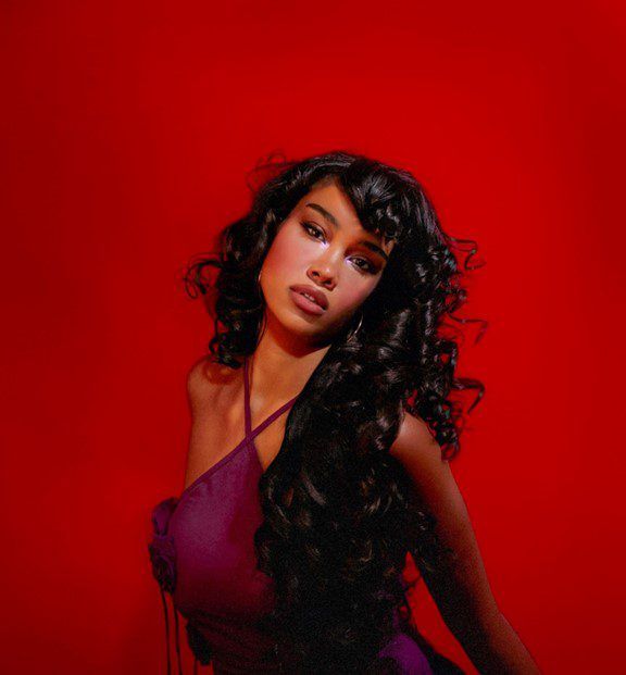 Portrait of a woman with curly dark hair in a purple dress against a vivid red background