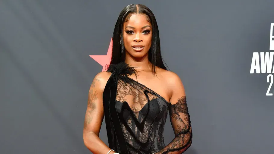 Woman in a black lace dress posing on a red carpet at an awards event.