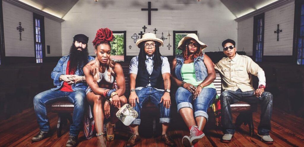Five people seated on chairs in a church sanctuary, posing under a large cross.