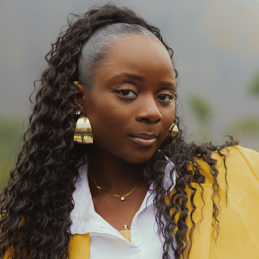 Portrait of a woman with curly hair in a yellow jacket and white shirt, wearing gold earrings.