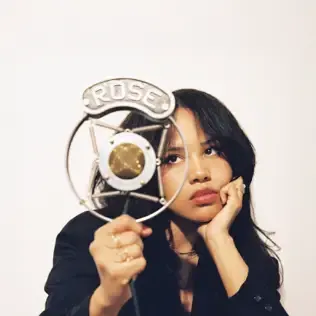 Woman holding a circular fan with “ROSE” lettering, resting her face on one hand against a white background