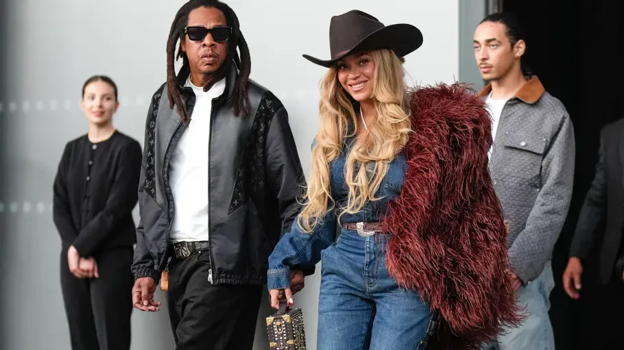 Four stylish people posing in a studio, including one in a black hat and one in a red fur jacket.