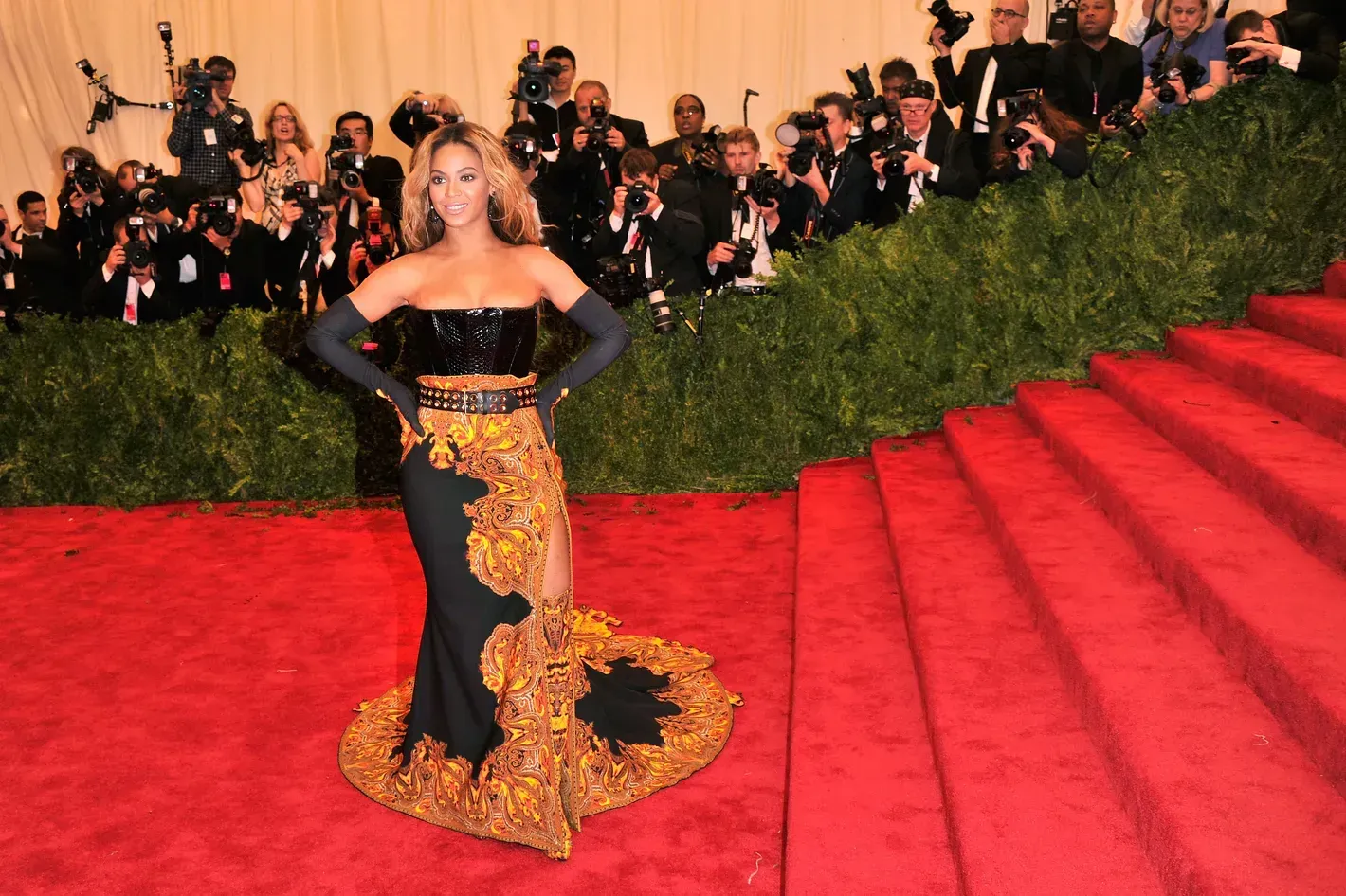 Woman in black-and-gold gown posing on a red carpet at a formal event