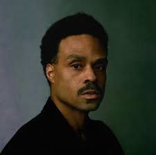 Portrait of a man with short dark hair and a mustache against a dark green background