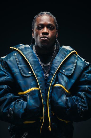 Portrait of a person in a blue jacket with yellow trim, standing against a dark background.