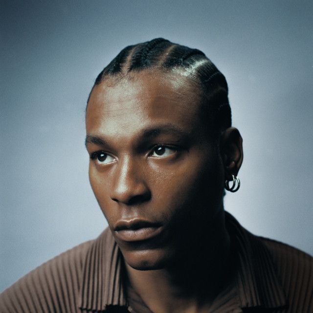 Portrait of a man with braided hair and hoop earring against a blue-gray background