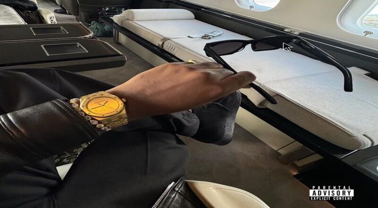 Person’s hand with gold watch resting on a car center console, with papers on the dashboard.