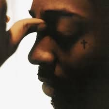 Close-up profile of a person with eyes closed, hand touching forehead, small cross tattoo under the eye.