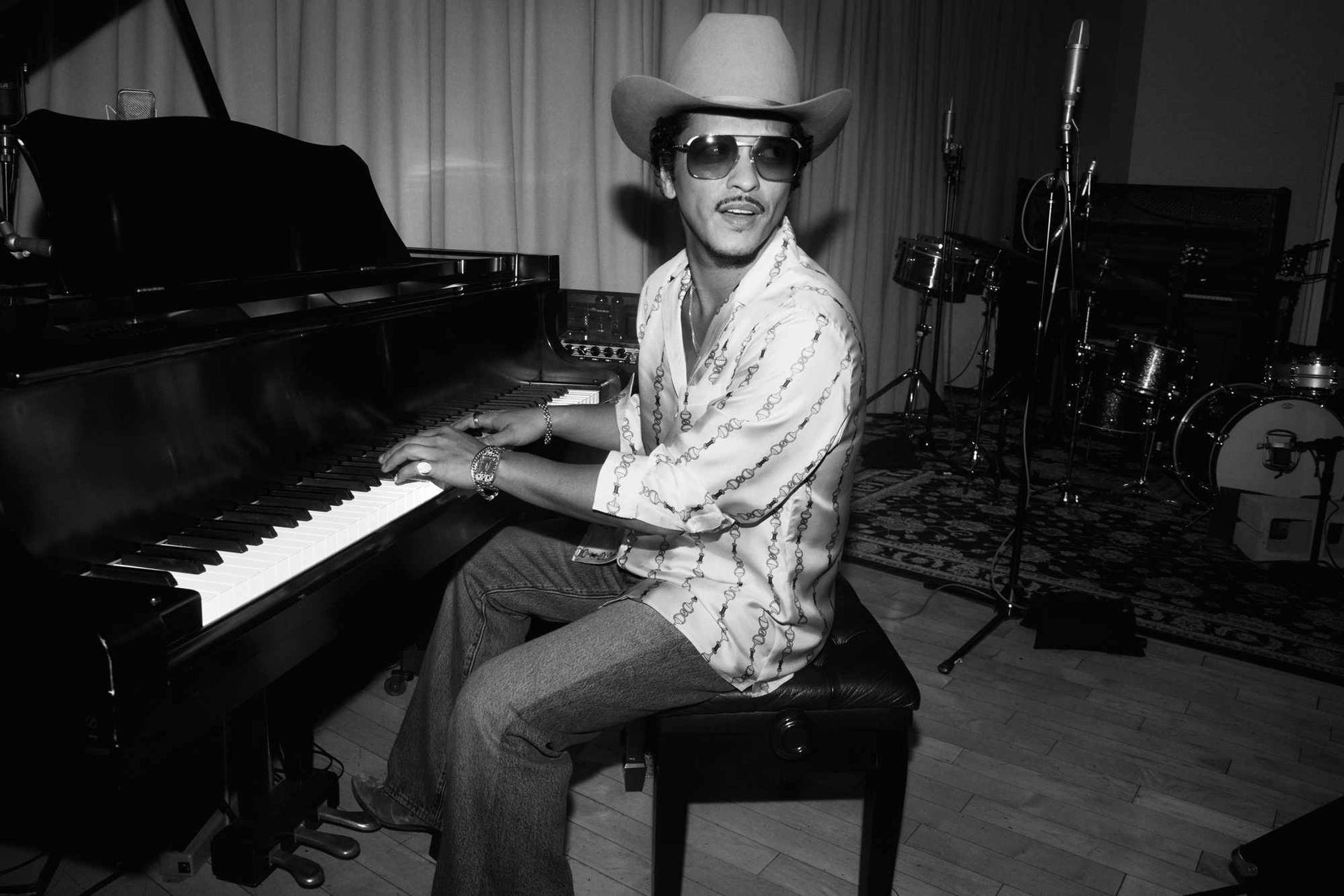 Man in cowboy hat seated at a piano in a music studio, smiling toward the camera