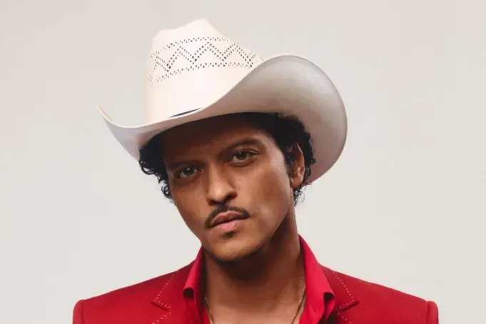 Person in a white cowboy hat and red shirt, looking at the camera against a plain background