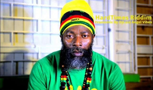 Man in green shirt and striped knit cap with beaded necklace, seated indoors against a window.