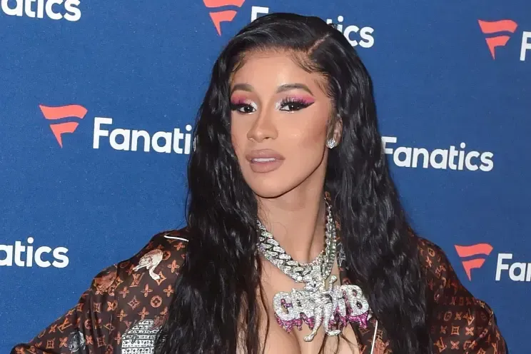 Woman with long black hair posing at a Fanatics event, wearing pink makeup and a diamond necklace.