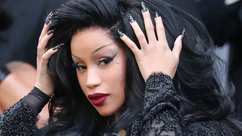 Woman with long black hair and red lipstick, posing with hands in her hair against a blurred background