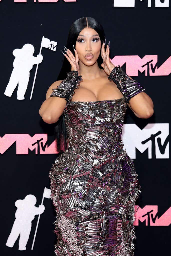 Woman in a sequined strapless dress posing on the MTV red carpet with hands near her face.